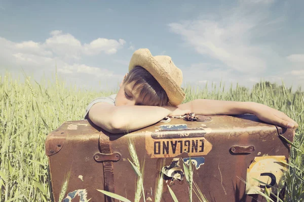 Young cowboy sleeps leaning against his suitcase in the middle of the prairie — Stock Photo, Image