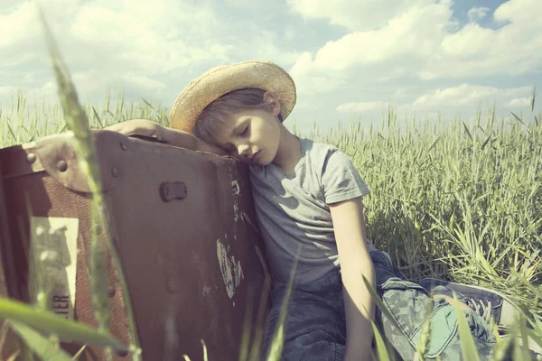 Jeune cow-boy se détend sur sa lourde valise dans une prairie — Photo