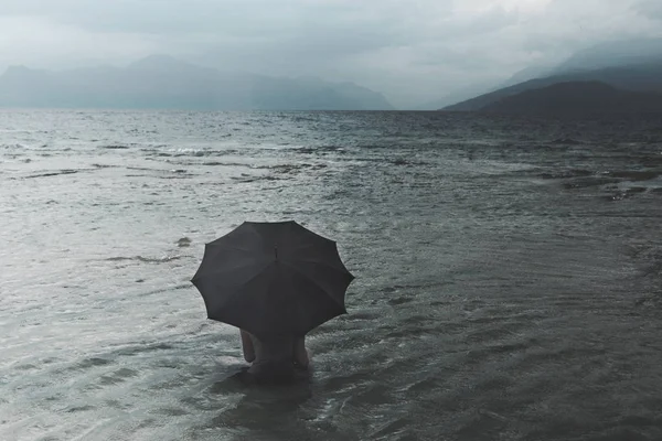 Denizde oturan yağmur bekliyor şemsiye ile yalnız kadın