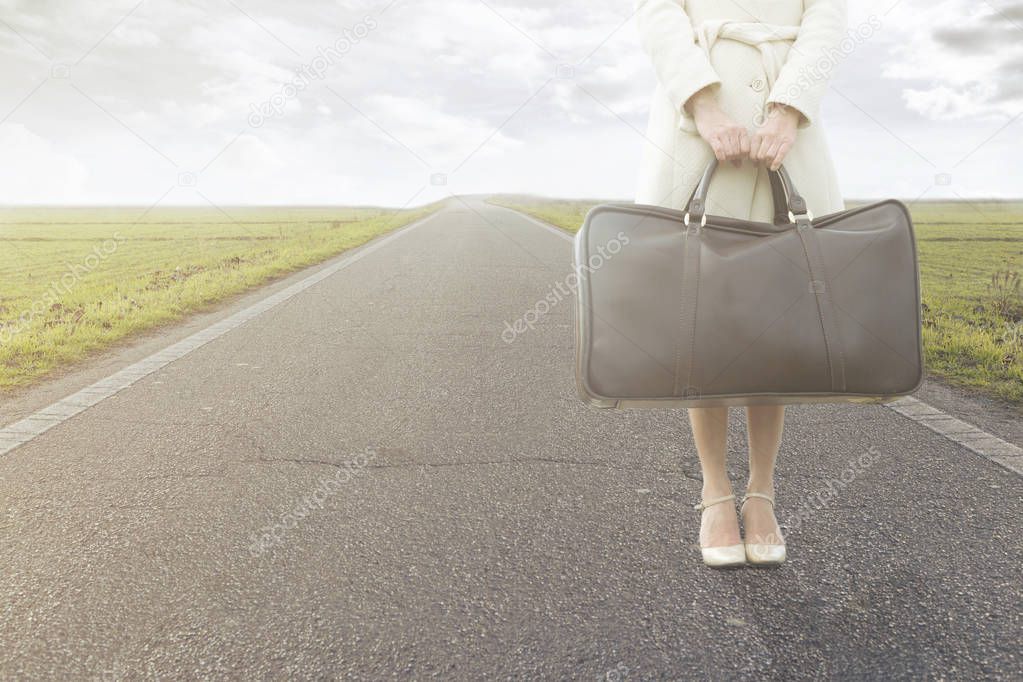 traveling woman waits with her suitcase on the roadside