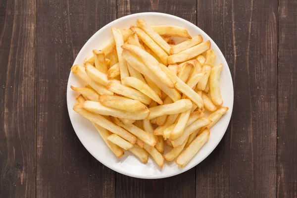 Batatas fritas no prato branco no fundo de madeira — Fotografia de Stock