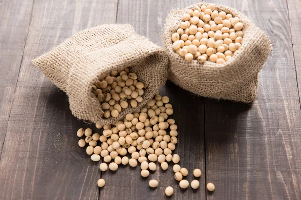 Soybean in a bag on wooden background. — Stock Photo, Image