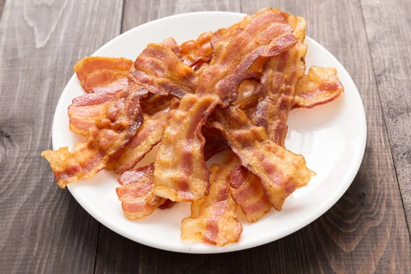 Closeup of fried bacon strips on white plate — Stock Photo, Image