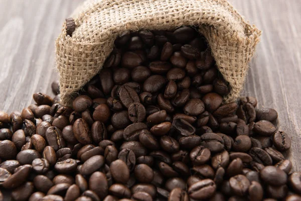 Grãos de café em um saco no fundo de madeira — Fotografia de Stock