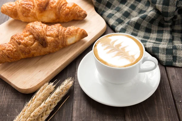 Snídaně šálek kávy a croissantu na dřevěný stůl — Stock fotografie