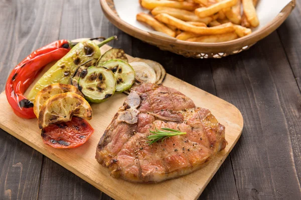 Carne de cerdo a la parrilla, verduras y patatas fritas en suelo de madera Imágenes de stock libres de derechos