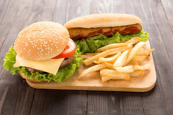 Cachorros-quentes, hambúrgueres e batatas fritas no fundo de madeira Imagem De Stock