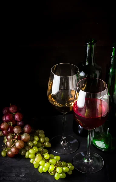 Вино в стаканах и различные сорта винограда на темном фоне . — стоковое фото