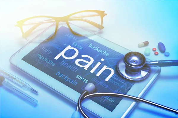 Palabra de dolor en la pantalla de la tableta con equipo médico en segundo plano —  Fotos de Stock