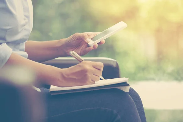 Femme d'affaires utilisant le téléphone intelligent mobile et l'écriture sur ordinateur portable — Photo