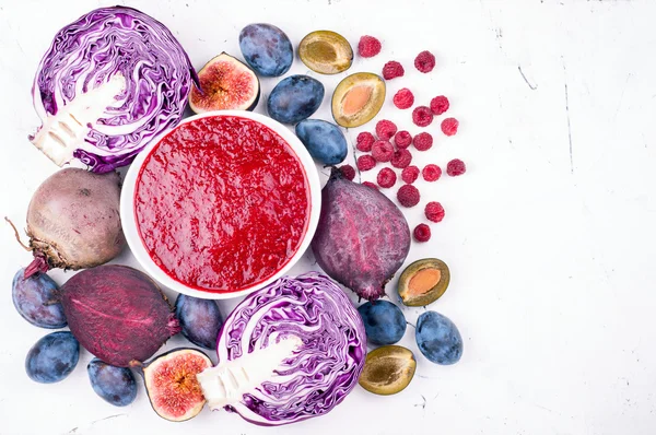 Smoothies bowl with purple fruit and vegetables on light background. Top view