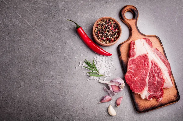 Viande crue sur fond de pierre sombre. Steak de boeuf cru sur planche à découper avec romarin, ail et épices. Espace de copie — Photo