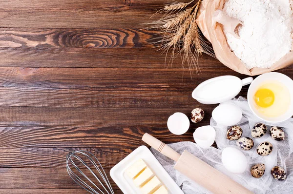 Antecedentes. Ingredientes para cozinhar. Farinha em saco de papel, ovos, manteiga, utensílios de cozinha sobre fundo de madeira. Espaço de cópia — Fotografia de Stock