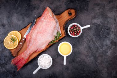 Taze balık ham snapper ile limon dilimleri, otlar biberiye, tuz ve biber taş koyu arka plan üzerinde. Sağlıklı gıda ve beslenme kavramı. Balık Pişirme için malzemeler