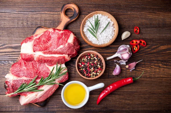 Raw meat. Raw beef steak on cutting board with rosemary, garlic and spices. Ingredients for cooking meat