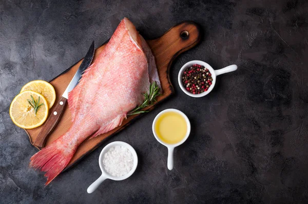 Taze balık ham snapper ile limon dilimleri, otlar biberiye, tuz ve biber taş koyu arka plan üzerinde. Sağlıklı gıda ve beslenme kavramı. Balık Pişirme için malzemeler