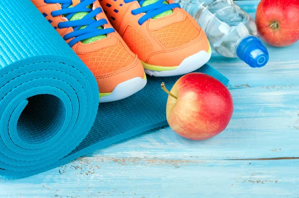 Tapete de ioga, sapatos esportivos, maçã, garrafa de água no fundo de madeira azul. Conceito de estilo de vida saudável, alimentação saudável, esporte e dieta. Equipamento desportivo — Fotografia de Stock