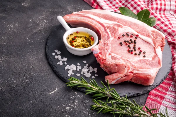 Syrové maso na tmavém pozadí. Surový Vepřový steak s bylinkami, oleje a koření. Vaření masa. — Stock fotografie