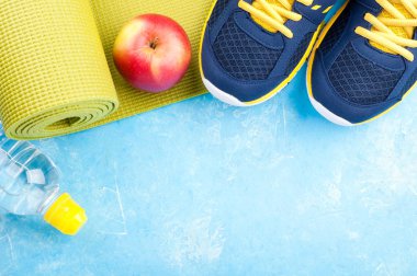 Yoga mat, spor ayakkabı, elma, şişe su koyu arka plan üzerinde. Kavram sağlıklı yaşam tarzı, sağlıklı gıda, spor ve diyet. Spor donatımı