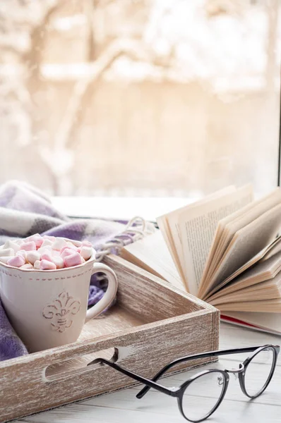 Кофейная чашка, открытая книга, стаканы, зефир и клетка на подоконнике зимой. Концепция теплого и уютного домашнего декора — стоковое фото