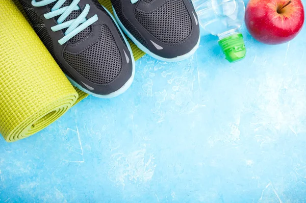 Esterilla de yoga, zapatos deportivos, manzanas, botella de agua sobre fondo azul. Concepto de estilo de vida saludable, comida saludable, deporte y dieta. Equipamiento deportivo — Foto de Stock