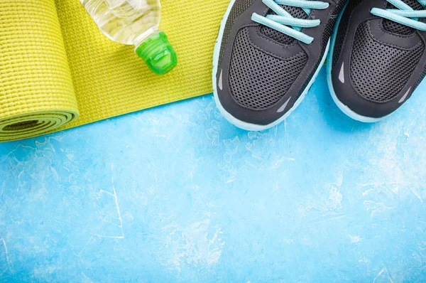 Yoga mat, sport shoes and bottle of water on blue background. Concept healthy lifestyle, sport and diet. Sport equipment