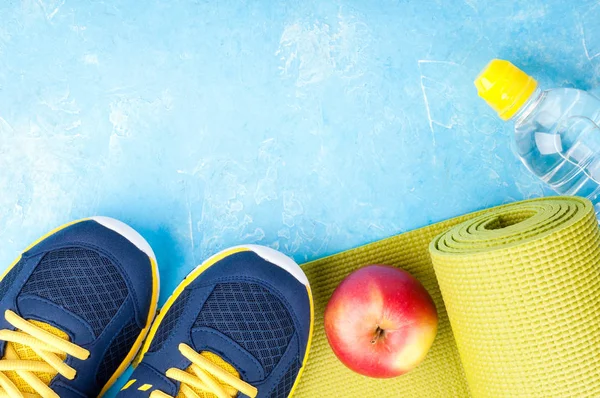 Yoga mat, sport shoes, apples, bottle of water on blue background. Concept healthy lifestyle, healthy food, sport and diet. Sport equipment