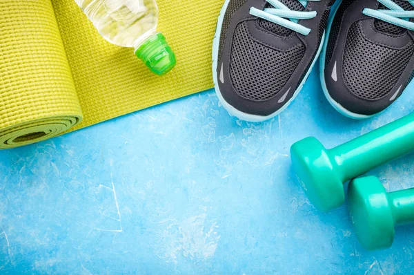 Esterilla de yoga, zapatos deportivos, mancuernas y botella de agua sobre fondo azul. Concepto de estilo de vida saludable, deporte y dieta. Equipamiento deportivo — Foto de Stock