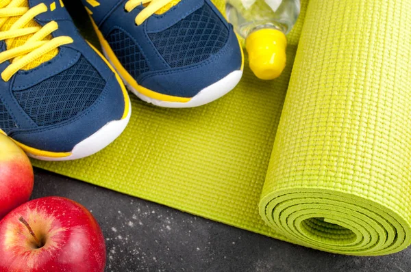 Yoga mat, sport shoes, apples, bottle of water on dark background. Concept healthy lifestyle, healthy eating, sport and diet. Sport equipment