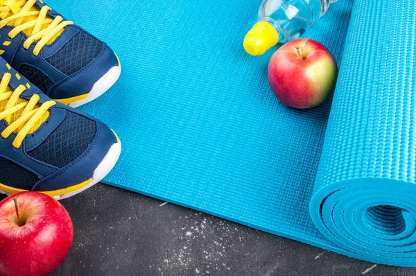 Yoga mat, sport shoes, apples, bottle of water on dark background. Concept healthy lifestyle, healthy eating, sport and diet. Sport equipment