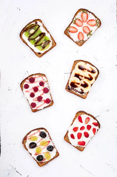 Здоровый завтрак с тостами. Сладкие сэндвичи со сливочным сыром и свежими ягодами и фруктами на белом фоне. Здоровое питание и диета — стоковое фото