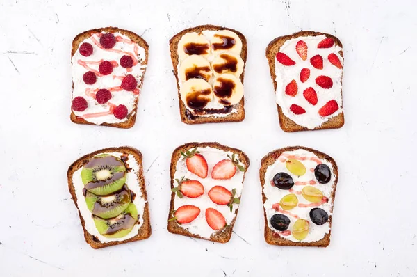 Тост за здоровый завтрак. Сладкие сэндвичи со сливочным сыром и свежими ягодами и фруктами на белом фоне — стоковое фото
