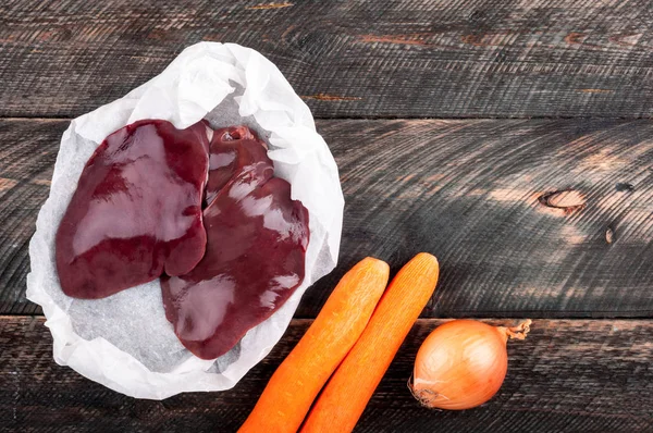 Rohe Leber und Gemüse Karotten und Zwiebeln auf dunklem Holzgrund. Zutaten zum Kochen von Leber oder Pastete — Stockfoto