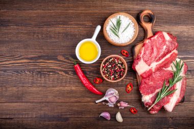 Otlar ve baharatlar ahşap zemin üzerine etli. Biberiye ve sarımsak ile kesme tahtası üzerinde ham sığır eti biftek. Et yemek pişirmek için malzemeler
