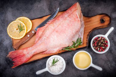 Balık ham snapper ile limon dilimleri, otlar biberiye, tuz ve biber koyu arka plan üzerinde. Sağlıklı gıda ve beslenme kavramı. Balık Pişirme için malzemeler