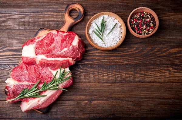 Otlar ve baharatlar ahşap zemin üzerine etli. Biberiye ve sarımsak ile kesme tahtası üzerinde ham sığır eti biftek. Et yemek pişirmek için malzemeler — Stok fotoğraf
