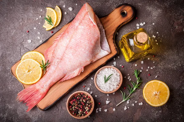 Fish raw snapper with lemon slices, herbs rosemary, salt and pepper on dark background. Healthy food and diet concept.  Ingredients for cooking fish