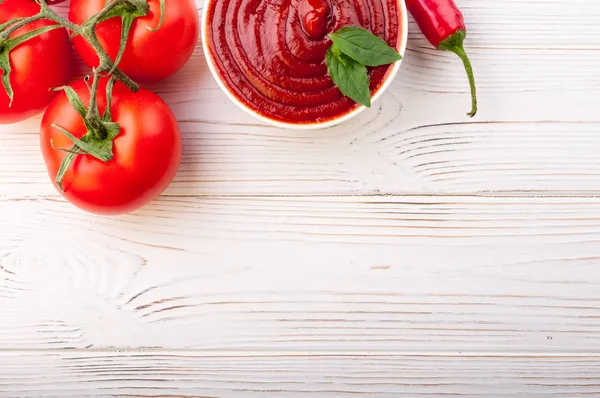 Tomatsås ketchup i en skål med chili, basilic och tomater. Ingredienser för matlagning ketchup på vit trä bakgrund — Stockfoto