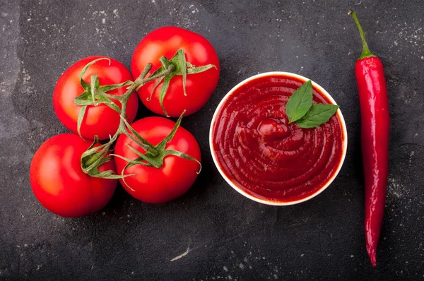 Tomatenketchup-Sauce in einer Schüssel mit Chili, Basilikum und Tomaten. Zutaten zum Kochen von Ketchup auf dunklem Hintergrund — Stockfoto