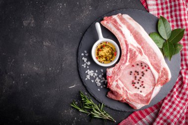 Çiğ et otlar, yağlar ve baharat koyu arka plan üzerinde ile. Çiğ domuz biftek. Et yemek pişirmek için malzemeler