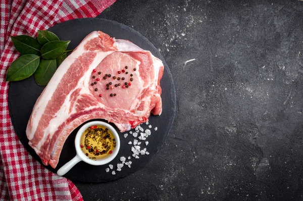 Çiğ et otlar, yağlar ve baharat koyu arka plan üzerinde ile. Çiğ domuz biftek. Et yemek pişirmek için malzemeler — Stok fotoğraf