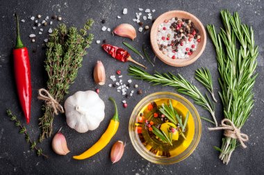 Otlar ve baharatlar. Biberiye, kekik, kırmızı biber, sarımsak, zeytinyağı, tuz ve biber karanlık masaya. Pişirme malzemeleri