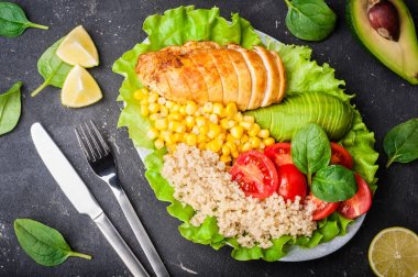 Sağlıklı yemek quinoa, tavuk, domates, avokado, ıspanak ve marul yaprakları. Koyu arka plan üzerinde sağlıklı salata kasesi. Dengeli gıda ve beslenme kavramı