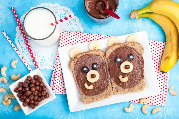 Café da manhã infantil com sanduíches e leite. Sanduíches de cara de urso engraçado com pasta de chocolate, banana, nozes e bagas — Fotografia de Stock