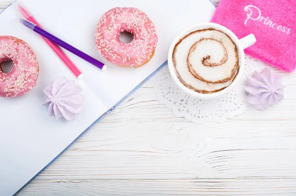 Женское рабочее место с чашкой кофе, альбомом эскизов, ручками, розовыми аксессуарами и пончиками — стоковое фото