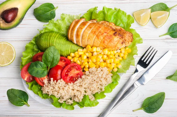 Healthy dinner with quinoa, chicken, tomatoes, avocado, spinach and lettuce leaves. Healthy salad bowl on white background. Balanced food and diet concept