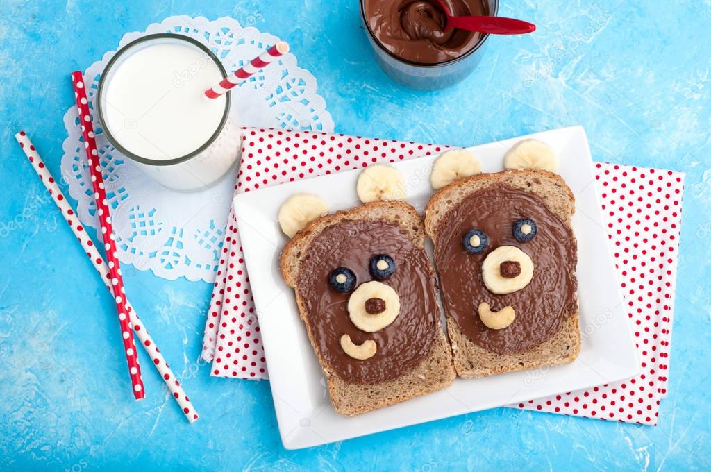 Children's breakfast with sandwiches and milk. Funny bear face sandwiches with chocolate paste, banana, nuts, and berries