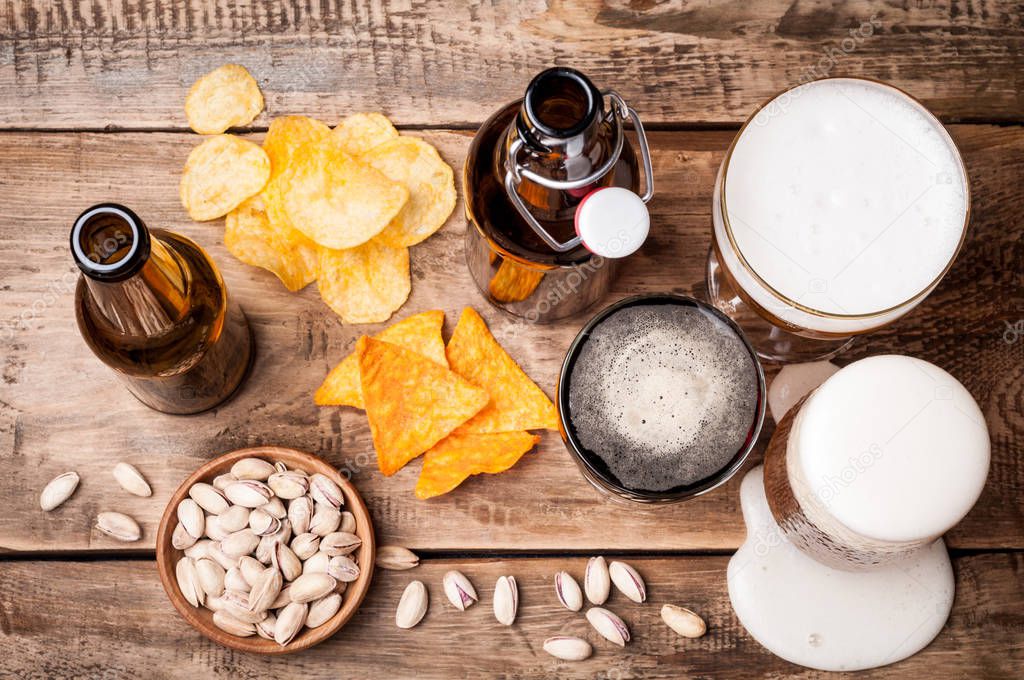 Beer in bottles and glasses on a wooden table. Beer and snacks are pistachio nuts, chips and nachos. Drink and snack for the football match or part
