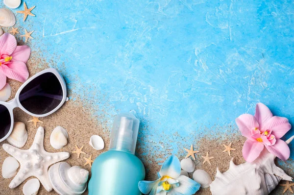 Літній святковий фон з сонцезахисними окулярами, сонцезахисним кремом, піском, мушлями та квітами. Пляжні аксесуари на блакитній поверхні зверху — стокове фото
