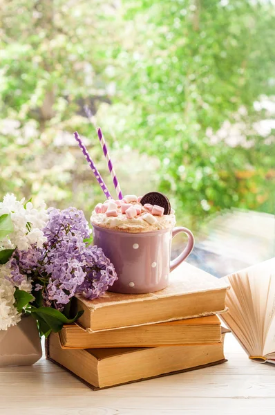 Kahvikuppi vaahtokarkki, avoin kirja ja kukkia kukkakimppu ikkunalaudalle. Aamiainen, lukeminen ja koulutus — kuvapankkivalokuva